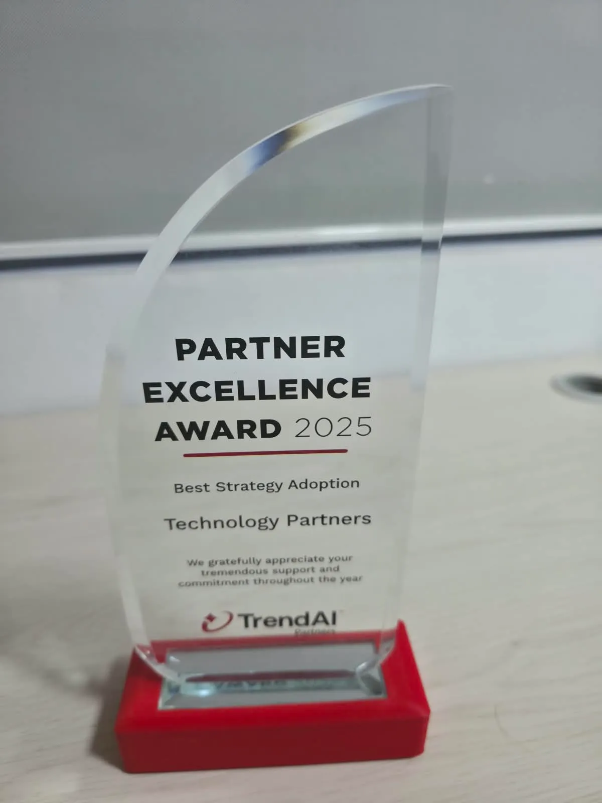 Galardón Partner Excellence Award 2025 en acrílico curvo sobre base roja, con la inscripción Best Strategy Adoption a nombre de Technology Partners y la marca TrendAI Partners.