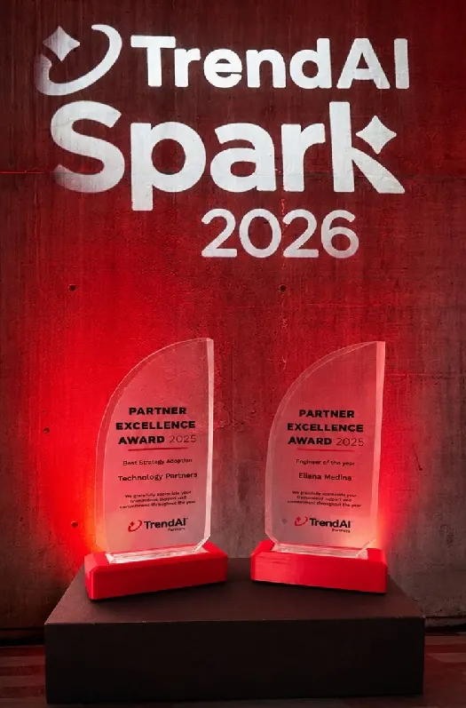 Dos galardones Partner Excellence Award 2025 de TrendAI sobre un pedestal, bajo el logotipo de TrendAI Spark 2026 proyectado en la pared.